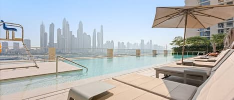 A rooftop pool area with lounge chairs and an umbrella, overlooking a city skyline.