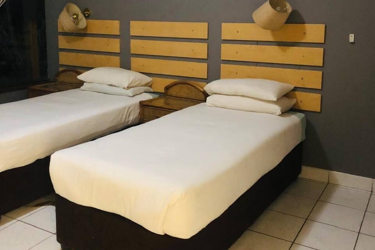 A hotel room with two beds, a wooden headboard, a small table, and a curtain.