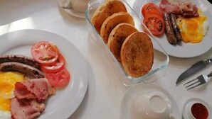 A breakfast table with plates of eggs, sausages, tomatoes, and pancakes. - Shelly Beach lodg  (Margate)