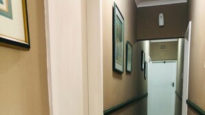 A corridor with beige walls, white trim, and marble flooring. There are framed pictures on the walls and a door at the end. - Shelly Beach lodg  (Margate)
