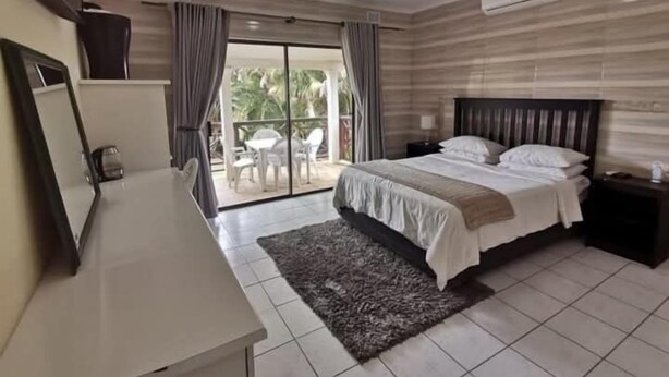 A hotel room with a bed, a desk, a chair, a small table, and a view of the outdoors. - Shelly Beach lodg  (Margate)