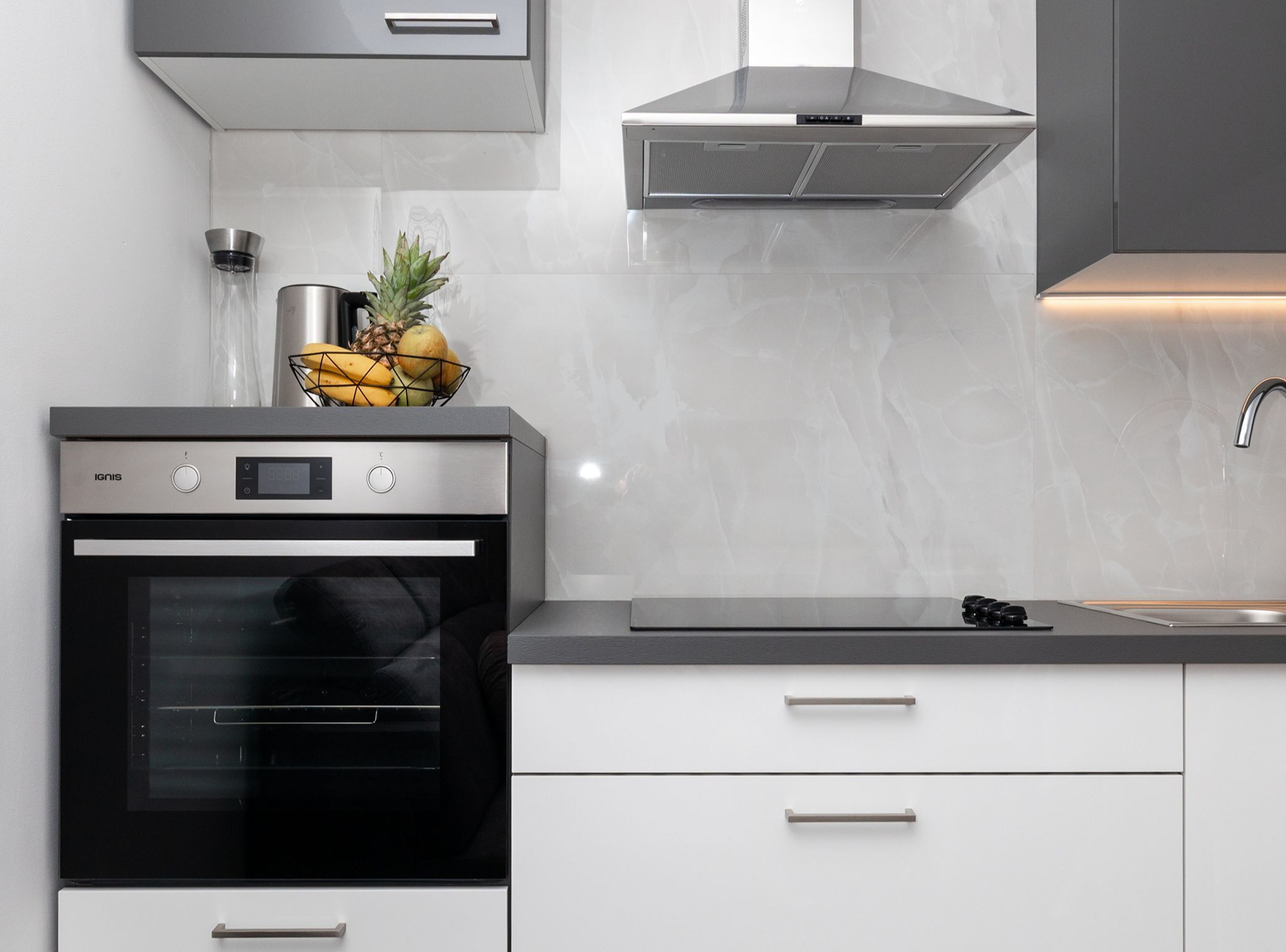 A modern kitchen with a built-in oven, stainless steel appliances, and a fruit bowl on the countertop.