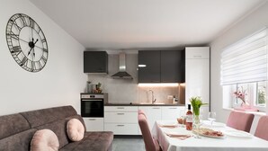 A modern kitchen with white cabinets, a built-in oven, and a large clock on the wall. - Apartment Kurte (Nerezise)