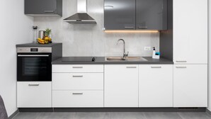 A modern kitchen with a built-in oven, a stainless steel range hood, a sink, and white cabinetry. - Apartment Kurte (Nerezise)