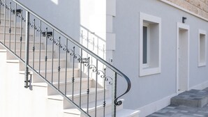 A staircase with ornate metal railings leading to a building with a light-colored exterior and a blue sign indicating the floor level. - Apartment Kurte (Nerezise)