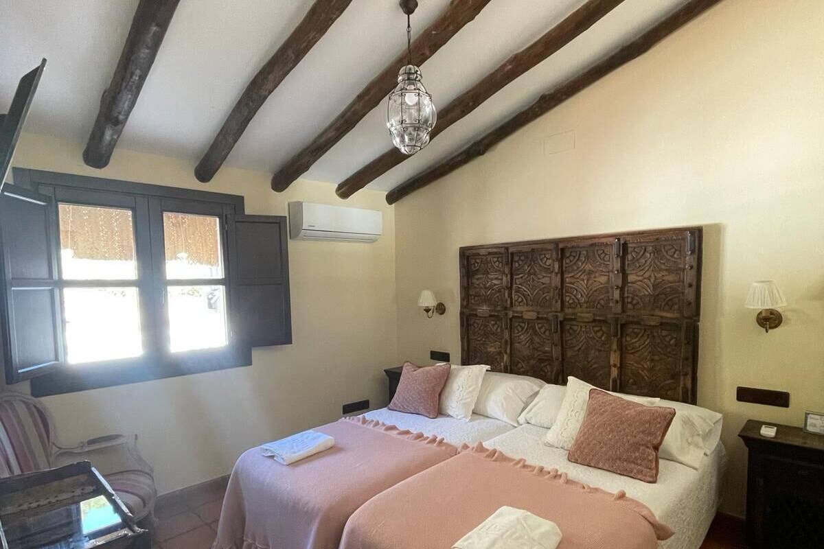Ein Schlafzimmer mit Holzboden, einem Bett mit zwei rosafarbenen Bettlaken, einem Holz-Kopfteil und einem kleinen Tisch mit einer Lampe.
