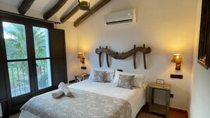 A bedroom with a large bed, wooden beams, a window with a view, an air conditioning unit, and bedside lamps. - Hotel Rural La Hacienda de Ronda  (Ronda)