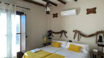 Una cama doble con ropa de cama amarilla y blanca, techo de madera y un equipo de aire acondicionado en la pared.