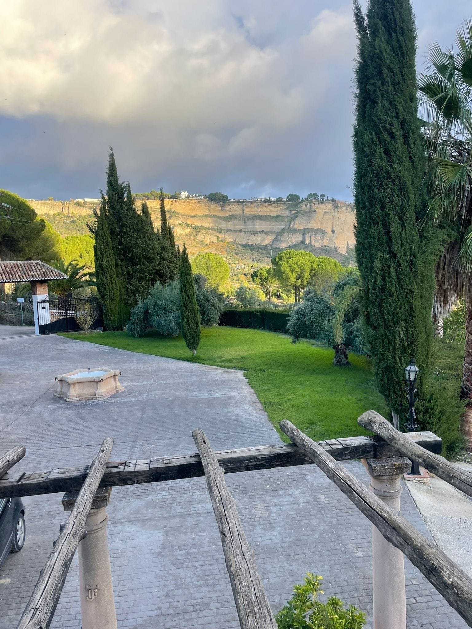 A courtyard with a fountain, a pergola, and a view of a mountainous landscape.