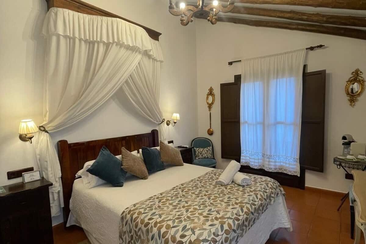Ein Schlafzimmer mit Bett, einer Deckenleuchte, einem Nachttisch, einem Sessel und einem Fenster mit Vorhängen.
