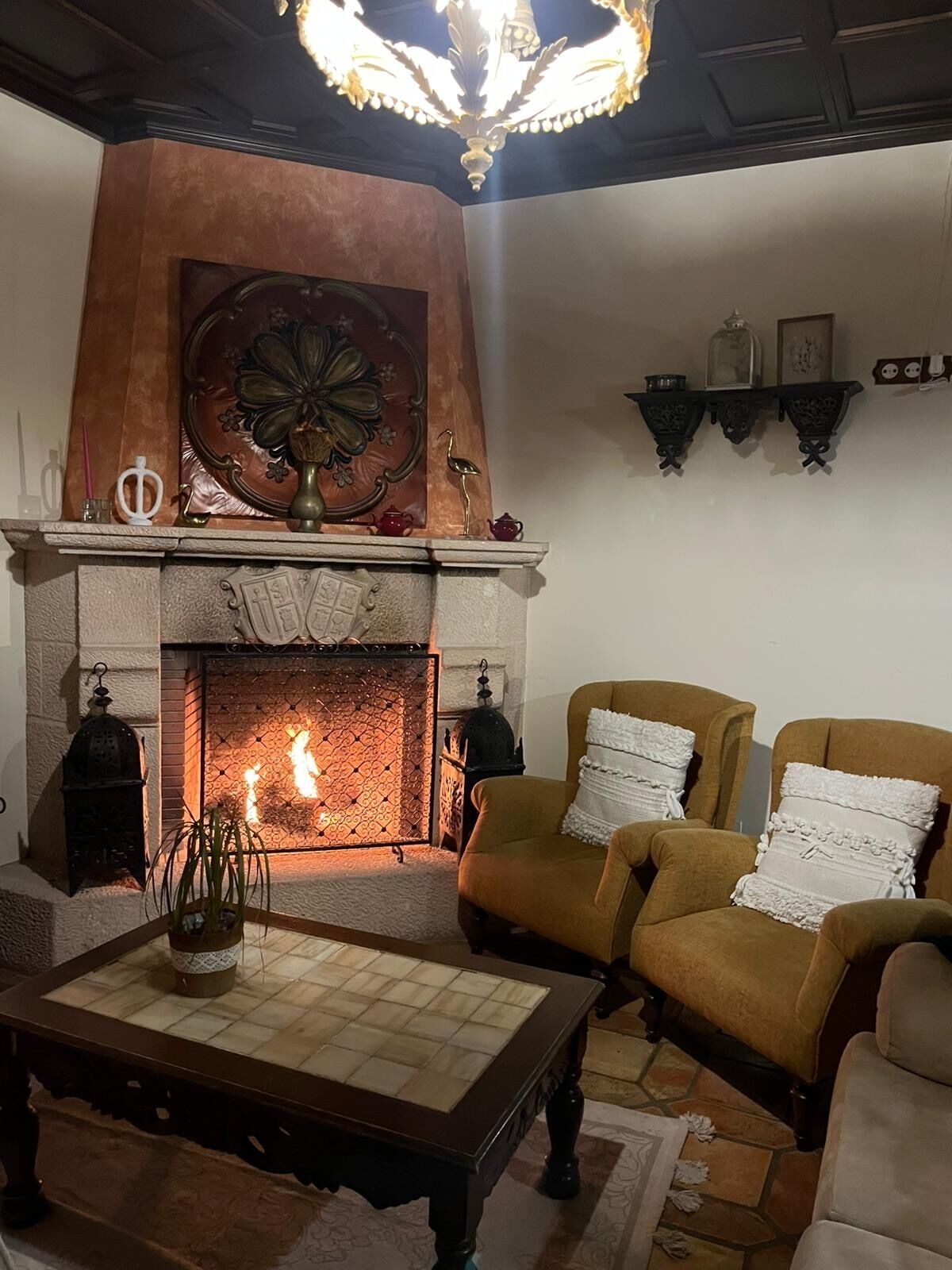 A cozy living room with a fireplace, two armchairs, a coffee table, and decorative items on the mantel.
