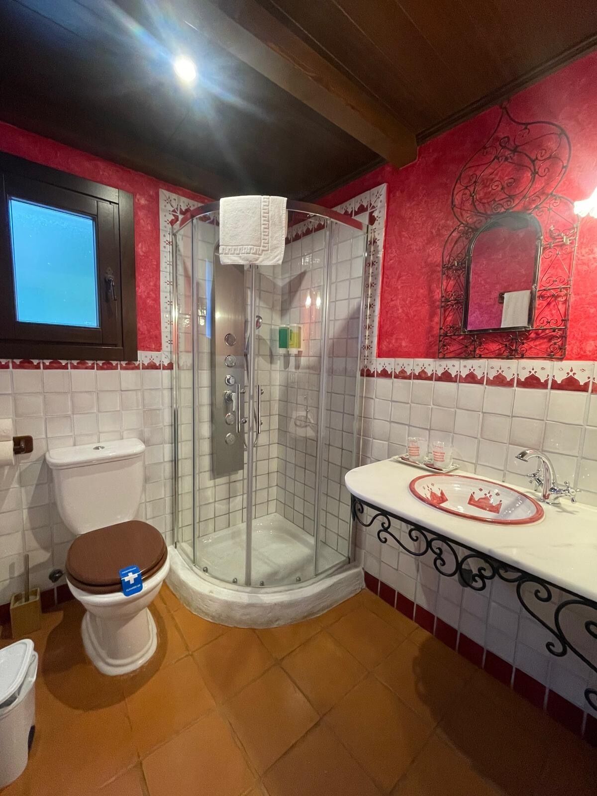 A bathroom with a glass-enclosed shower, a toilet with a brown seat, and a sink with a decorative basin.