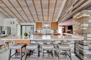 Una cocina moderna con una isla grande, vigas de madera en el techo y detalles de piedra.