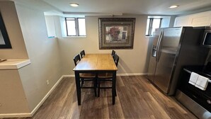 Un coin repas avec une table et des chaises en bois, un réfrigérateur et un tableau accroché au mur.