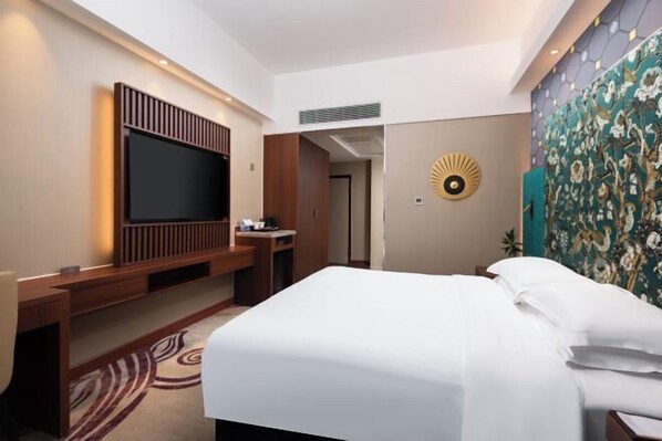 A hotel room with a bed, a TV mounted on the wall, a desk, and a decorative wall panel.