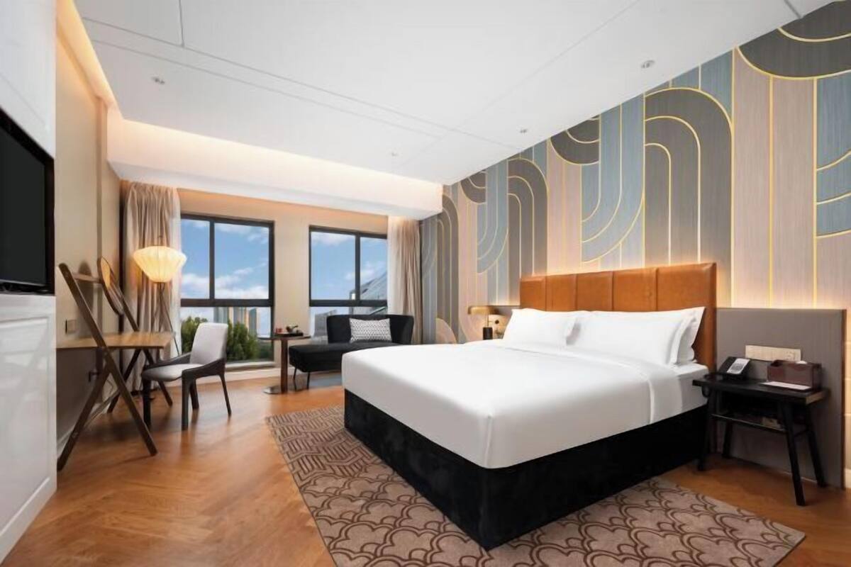 A hotel room with a large bed, a desk, a chair, and a view of the outdoors.