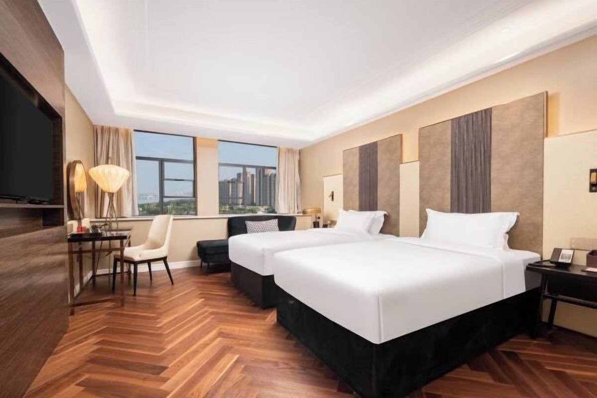 A hotel room with two beds, a desk, a chair, and a large window.