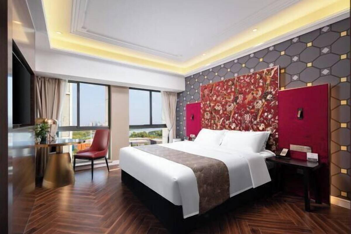 A modern hotel room with a large bed, a desk, and a view of the outdoors.