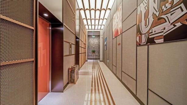 A hallway with a patterned floor, a red accent wall, and a ceiling with a unique light fixture. - Jinjiang Metropolo Hotel Wuhan Sports Center Subway Station Wanda Plaza (Wuhan)
