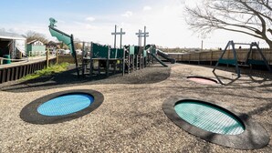 Een speeltuin met een glijbaan, schommels en twee ronde speelzones.