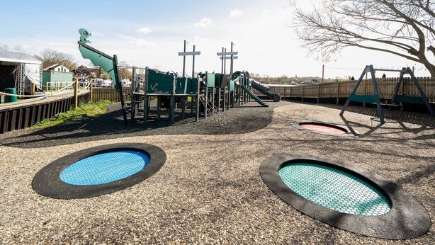 Een speeltuin met een glijbaan, schommels en twee ronde speelzones.