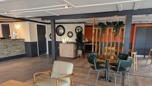 A spacious indoor area with a reception desk, a seating area with wooden and green chairs, and a counter with a coffee machine. - Nature's Nook - Billing Aquadrome (Northampton)