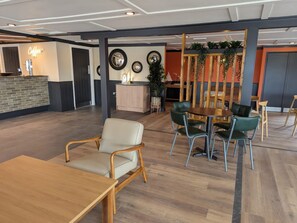 A spacious indoor area with a reception desk, a seating area with wooden and green chairs, and a counter with a coffee machine. - Nature's Nook - Billing Aquadrome (Northampton)