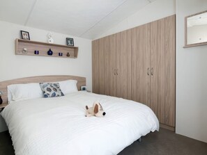 Un dormitorio con una cama, un armario de madera, una estantería con adornos y un espejo montado en la pared.