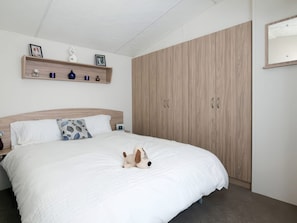 Ein Schlafzimmer mit einem Bett, einem Holzschrank, einem Regal mit Dekoration und einem Wandspiegel.