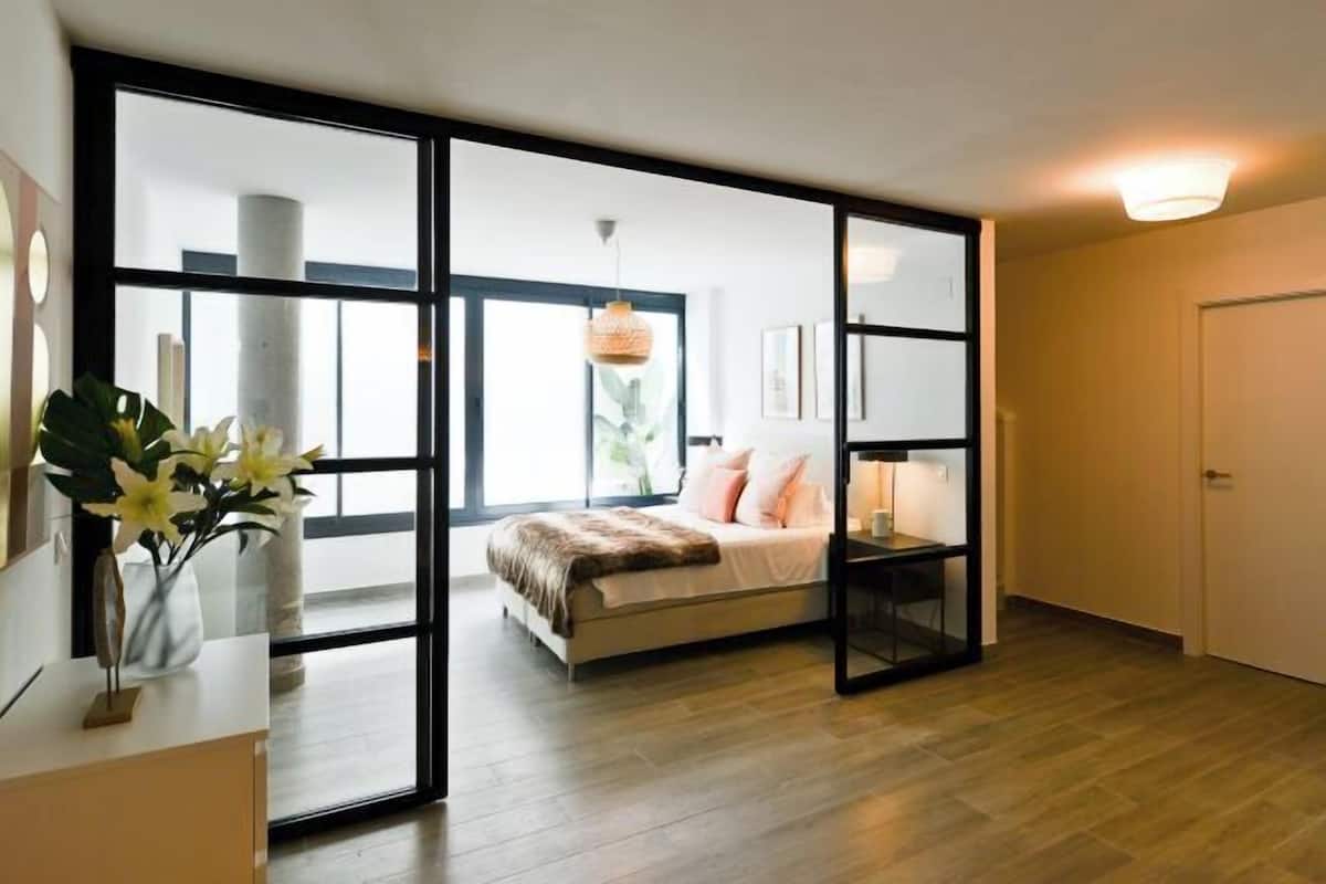 Ein modernes Schlafzimmer mit einem großen Bett, einem Nachttisch, einem Beistelltisch und einem Fenster mit Blick nach draußen.