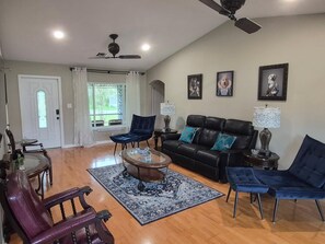 A spacious living room with a black leather sofa, blue chairs, a coffee table, and a patterned rug.