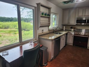 Una cocina con un ventanal grande, encimera de granito, electrodomésticos de acero inoxidable y vistas a zonas verdes.
