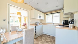 Een kleine keuken met een eethoek, met een visgraatvloer, witte kastjes en een raam dat voor natuurlijk licht zorgt.