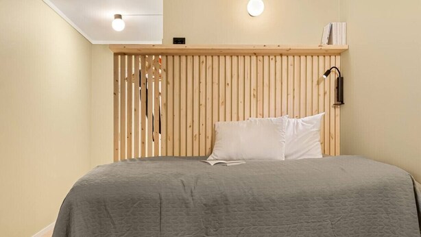 Un dormitorio con cabecera de madera, colcha acolchada gris y lámpara de noche.