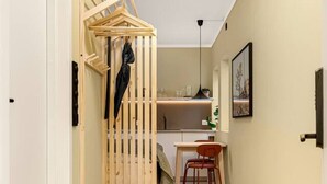 Un pasillo con una cama litera de madera, una zona de comedor con mesa y sillas, y un área de cocina al fondo.