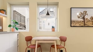 Una cocina con una mesa de comedor y sillas, una lámpara colgante y un ventanal con vistas a una casa y un paisaje desértico.