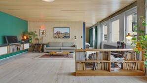 A modern living room with a wooden ceiling, a grey sofa, a coffee table, a bookshelf, and a TV on a stand.