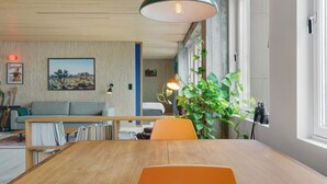 A modern living room with a wooden dining table, a sofa, and a large window.