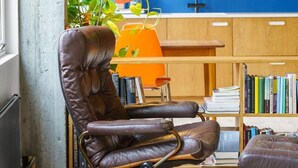 A modern kitchen with a blue accent wall, a leather chair, a dining table, and a bookshelf filled with books.
