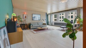A modern living room with a wooden ceiling, a grey sofa, a coffee table, and a large window offering a view of buildings.