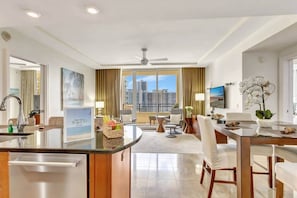 Una habitación de hotel moderna con cocina, mesa de comedor, sofá y televisor.