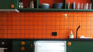 Una cocina con gabinetes verdes, azulejos naranjas y un refrigerador con puerta de vidrio.