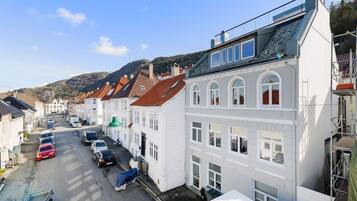 A row of white buildings with red roofs, parked cars, and a clear sky.