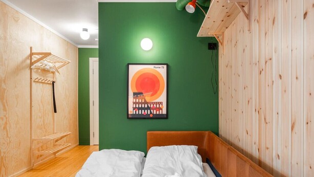 Una habitación con una cama, un tendedero de madera y un cuadro de Roma en la pared.