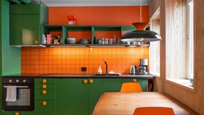 Una cocina con armarios verdes, salpicadero naranja y una mesa de madera.