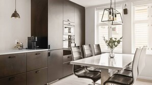 Una cocina moderna con armarios oscuros, una mesa de comedor blanca y sillas de cuero.