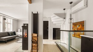Una sala de estar moderna con chimenea, una escalera y barandilla de cristal con vistas a un balcón.