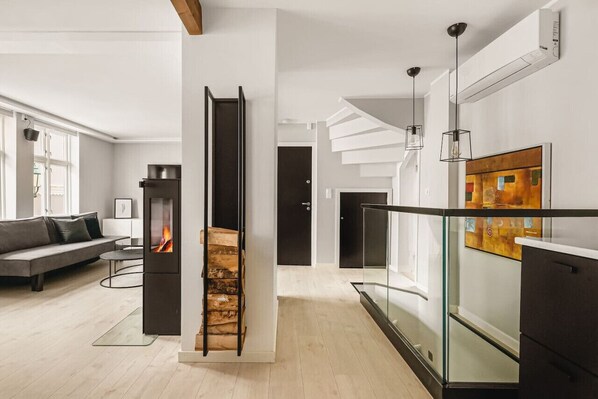 Ein modernes Wohnzimmer mit Kamin, einer Treppe und einem Glasgeländer mit Blick auf einen Balkon.