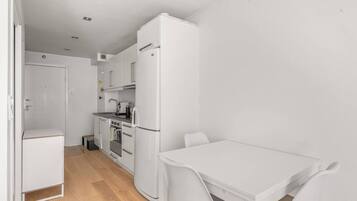 A compact kitchen with white appliances, a small oven, and a sink. There is a white table and chair set in the dining area.
