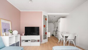A modern, well-lit room with a flat-screen TV, a desk, and a dining area.